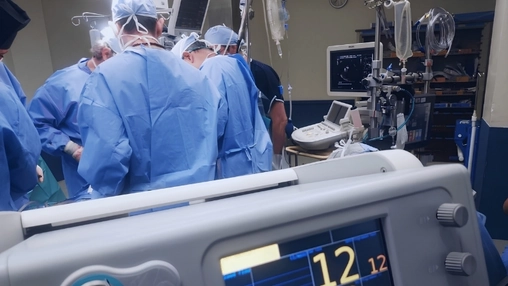Medical team performs surgery in a hospital theatre with diagnostic screens and equipment