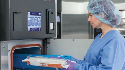 Healthcare worker loads a packaged medical item into a sterilization machine in a clean facility