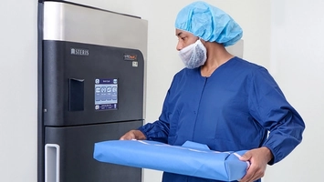 Healthcare worker in scrubs loading sterile pack into STERIS unit