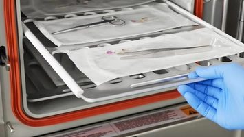 Gloved hand loading a sealed sterile instrument pack into a low-temperature chemical gas steriliser unit