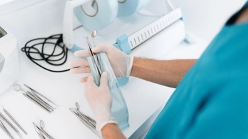 Clinician in blue scrubs and white gloves handling sterilised instrument pouches on a clinical workstation